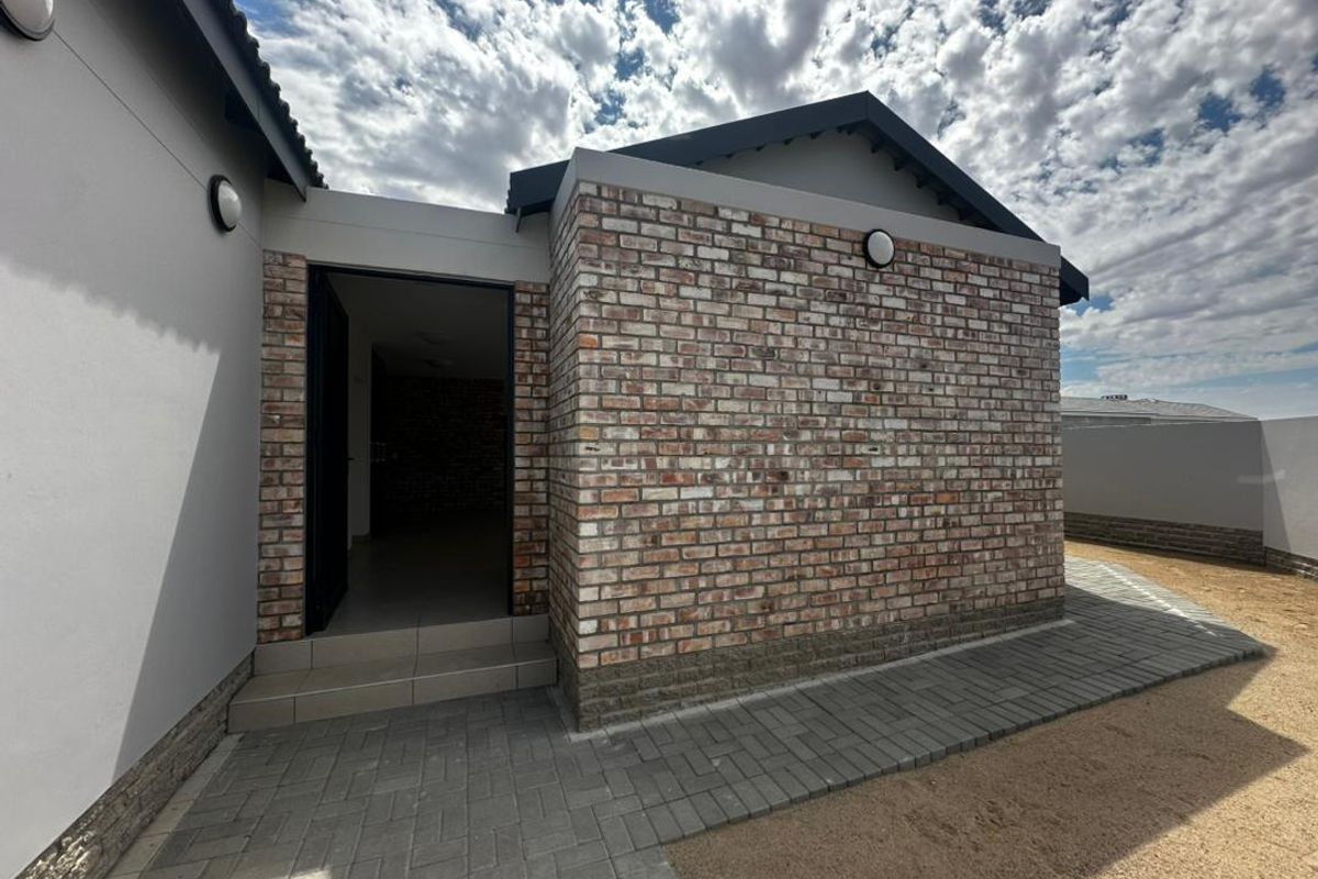 A modern rear exterior view featuring a clean exposed brick facade, paved walkway, and a tiled entrance step leading into the home.