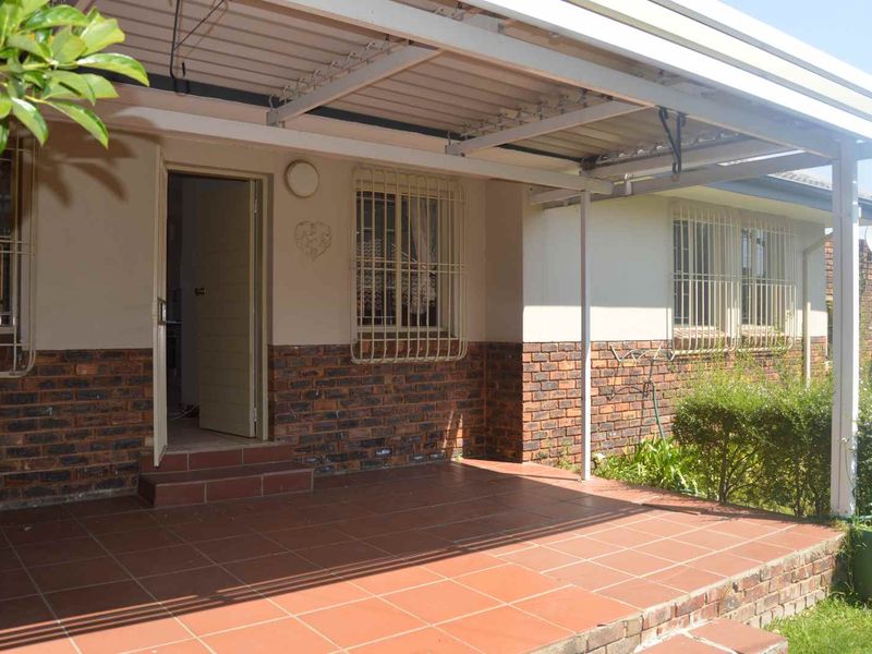A covered outdoor patio area featuring tiled flooring, brick exterior detailing, and security bars on the windows.
