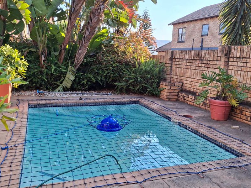 Outdoor pool area featuring a paved surround and brick boundary wall, equipped with a safety net.