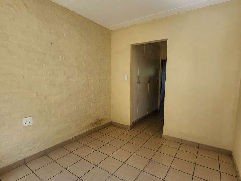 An empty bedroom featuring tiled flooring, an exposed brick feature wall, and built-in cupboards, offering a blank canvas for renovation.