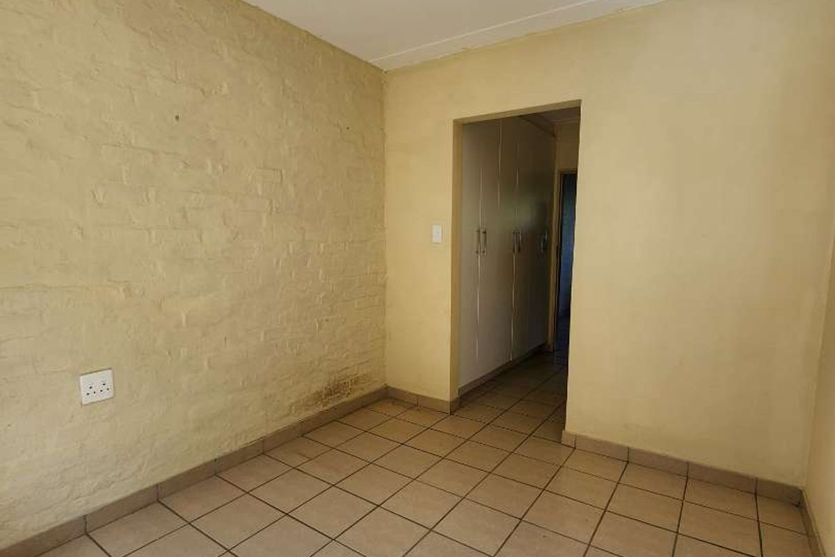 An empty bedroom featuring tiled flooring, an exposed brick feature wall, and built-in cupboards, offering a blank canvas for renovation.