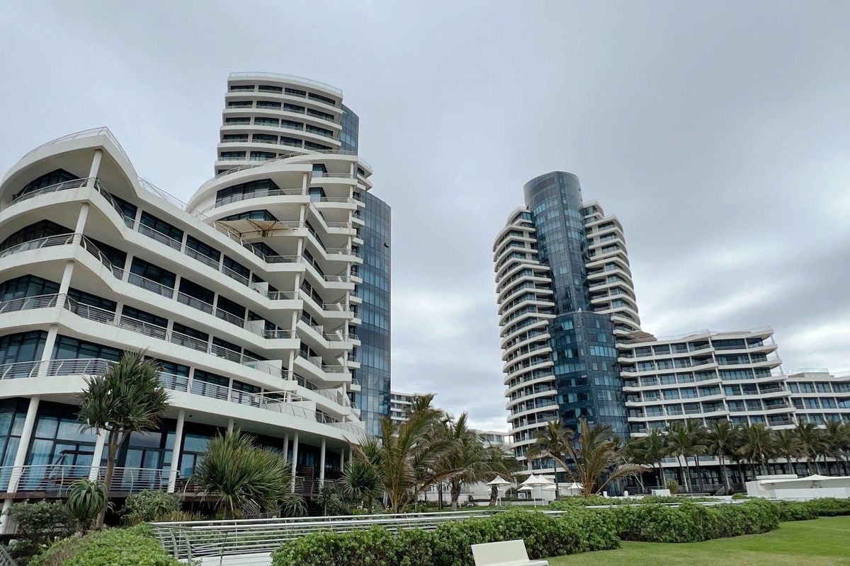 A view of the rear elevation of modern high-rise apartment towers featuring extensive balconies, glass facades, and well-maintained landscaped garden areas.