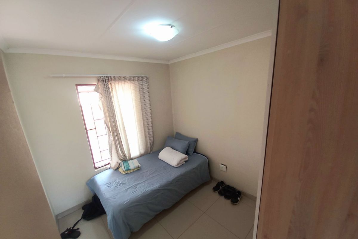A compact bedroom featuring tiled flooring, a window with security bars, and a built-in cupboard.