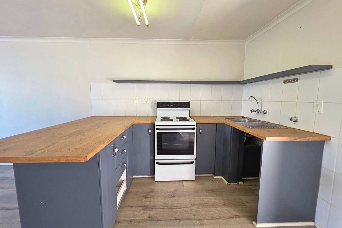A functional kitchen featuring wooden countertops, a freestanding stove, and a stainless steel sink with tiled splashback and open shelving.