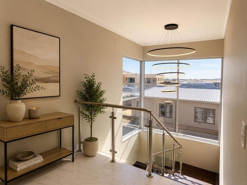 A bright and modern landing area featuring a contemporary multi-tier ring pendant light, stainless steel and glass balustrade, and large corner windows.