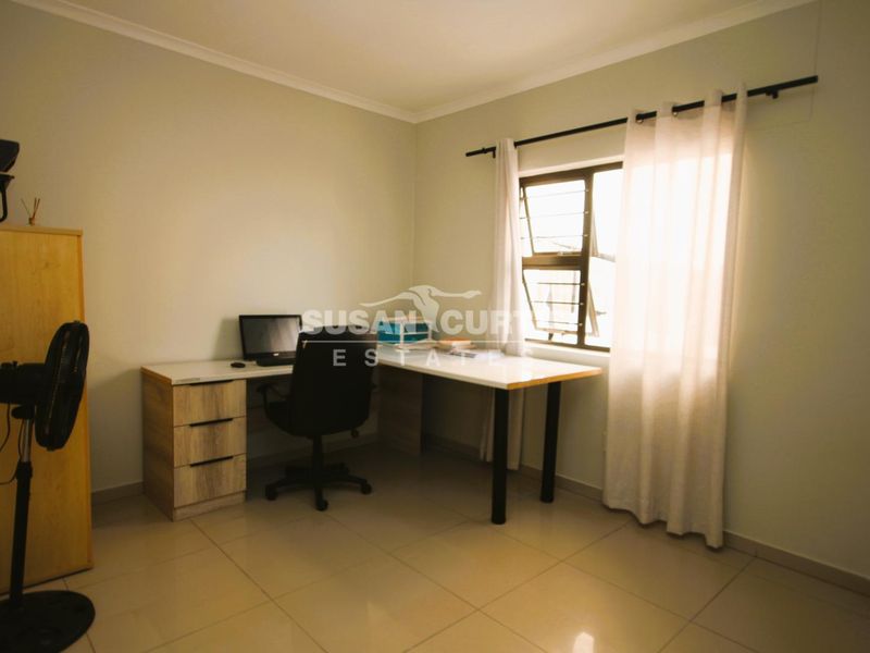 A functional home office space featuring tiled flooring and a window with security bars, providing a practical area for work or study.
