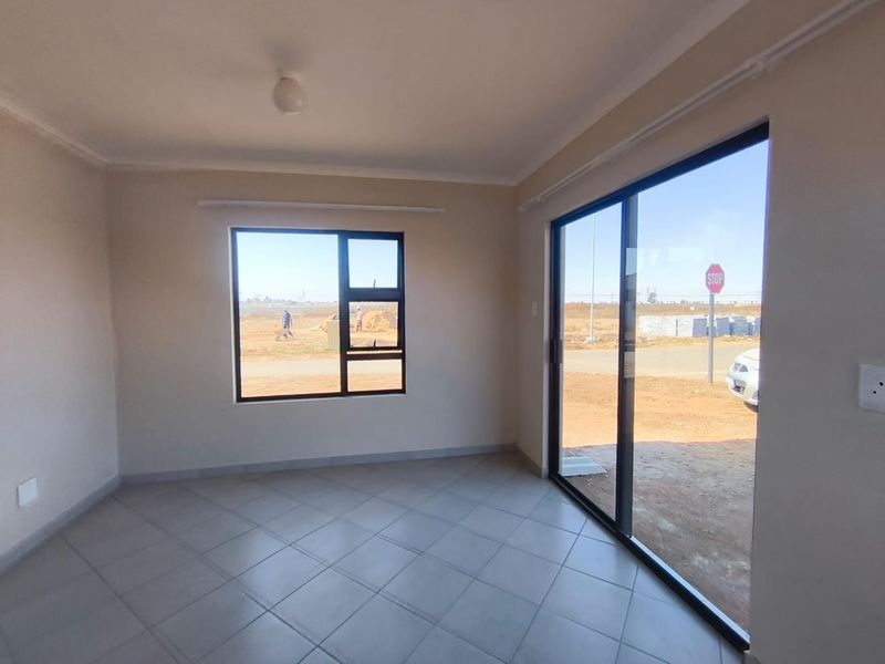 A bright, empty living room featuring tiled flooring, aluminium window frames, and a sliding door leading to the exterior.