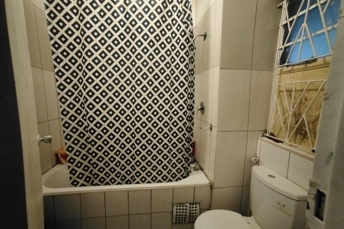 A compact bathroom featuring a bathtub with shower mixer, toilet, and tiled walls, requiring maintenance and cosmetic updates to improve its overall condition.