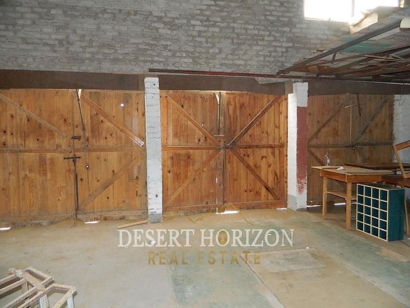 A spacious, unfinished garage area featuring exposed brick walls, concrete flooring, and large timber swing doors.