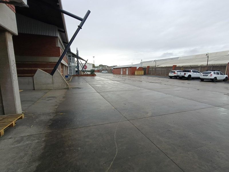 Spacious industrial concrete yard area featuring brick building facade, steel structural supports, and perimeter fencing, suitable for logistics or storage operations.