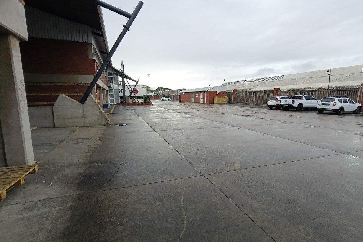 Spacious industrial concrete yard area featuring brick building facade, steel structural supports, and perimeter fencing, suitable for logistics or storage operations.
