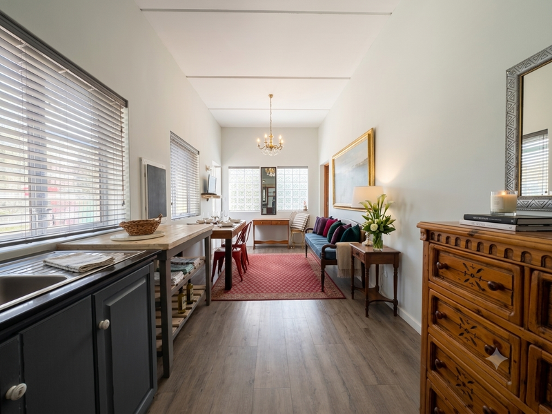 An open-plan living and kitchen area featuring laminate flooring, modern cabinetry, and a combination of venetian and glass block windows for natural light.