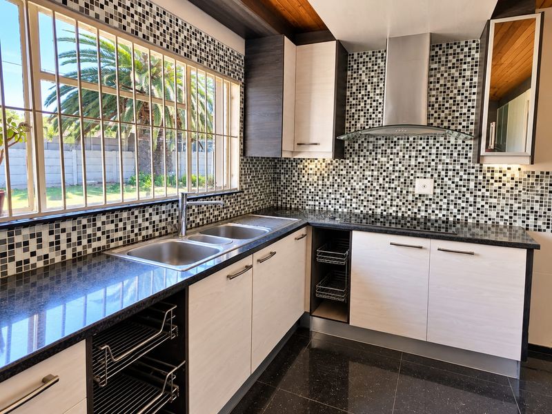 Modern kitchen featuring granite countertops, mosaic tile backsplash, stainless steel sink, extractor fan, and ample built-in cabinetry with pull-out storage solutions.