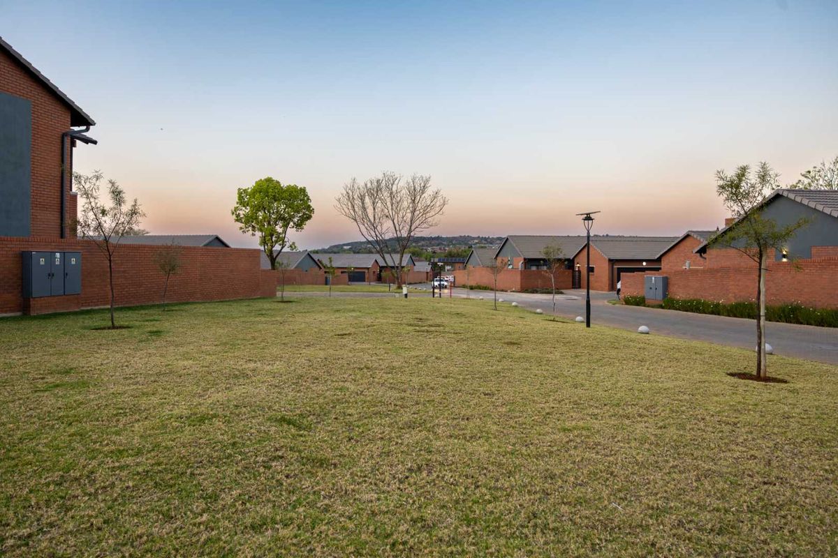 A view of the communal garden area and paved driveway within a residential apartment complex, featuring brick boundary walls and well-maintained landscaping.