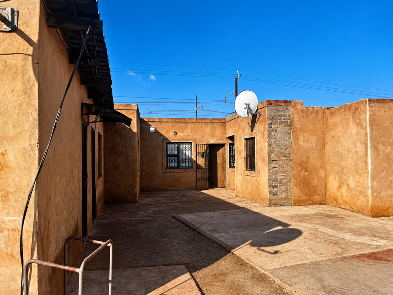 Rear courtyard area featuring concrete paving, security gates, and exterior walls with a textured finish.