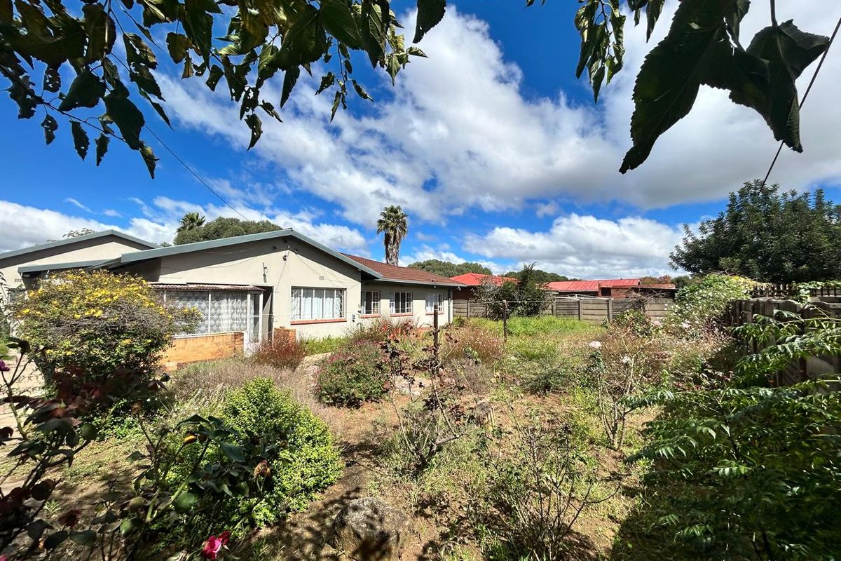 A view of the rear exterior of the house featuring a large, overgrown garden area and established landscaping.