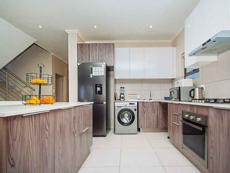 Modern kitchen featuring wood-grain cabinetry, stone countertops, integrated stainless steel appliances, and tiled flooring, with an adjacent staircase visible.