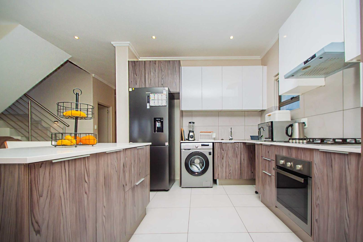 Modern kitchen featuring wood-grain cabinetry, stone countertops, integrated stainless steel appliances, and tiled flooring, with an adjacent staircase visible.