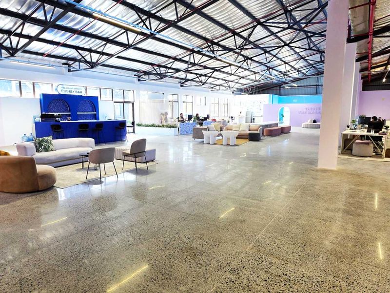 Spacious open-plan industrial warehouse conversion featuring polished concrete floors, exposed steel roof trusses, and a built-in bar area with modern architectural arches.
