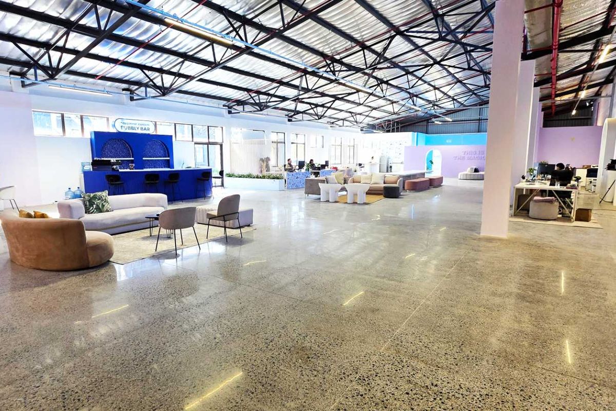 Spacious open-plan industrial warehouse conversion featuring polished concrete floors, exposed steel roof trusses, and a built-in bar area with modern architectural arches.