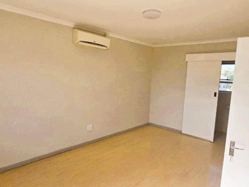 A clean, empty bedroom featuring light-toned laminate flooring, a wall-mounted split-system air conditioner, and a sliding door leading to an adjacent space.