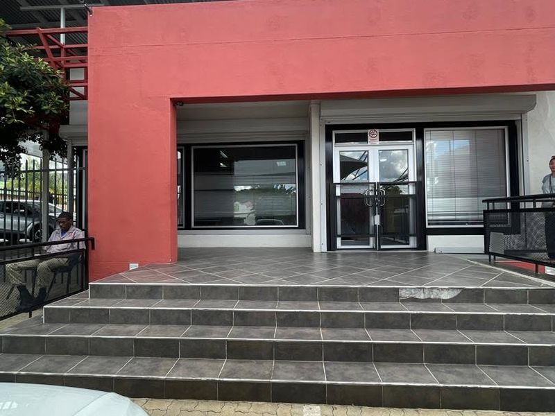 Front entrance of a commercial property featuring tiled steps, large display windows, and a metal-framed glass door with a paved parking area.