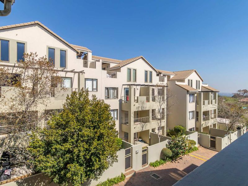 A multi-story apartment complex featuring a tiled roof, private balconies, and a paved driveway entrance.