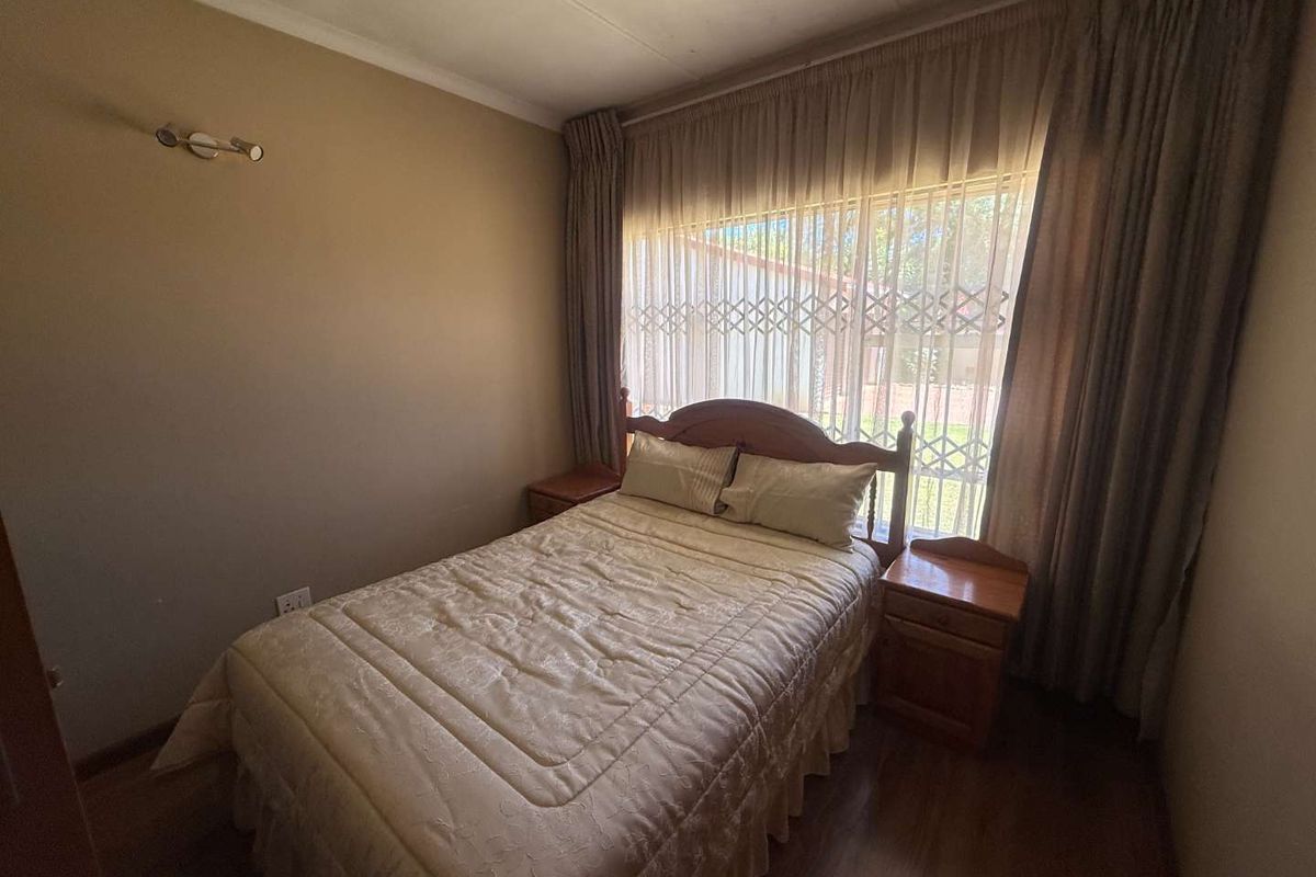 A cozy bedroom featuring laminate flooring and a large window fitted with a security gate and curtains.