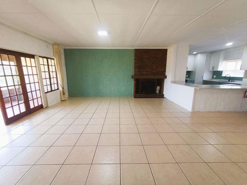 Spacious open-plan living area featuring tiled floors, a brick fireplace, and a breakfast bar connecting to the kitchen.
