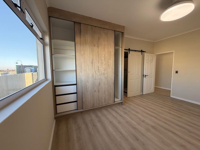 A bright, modern bedroom featuring light wood-look laminate flooring, a large built-in sliding wardrobe, and a stylish barn door leading to an en-suite.