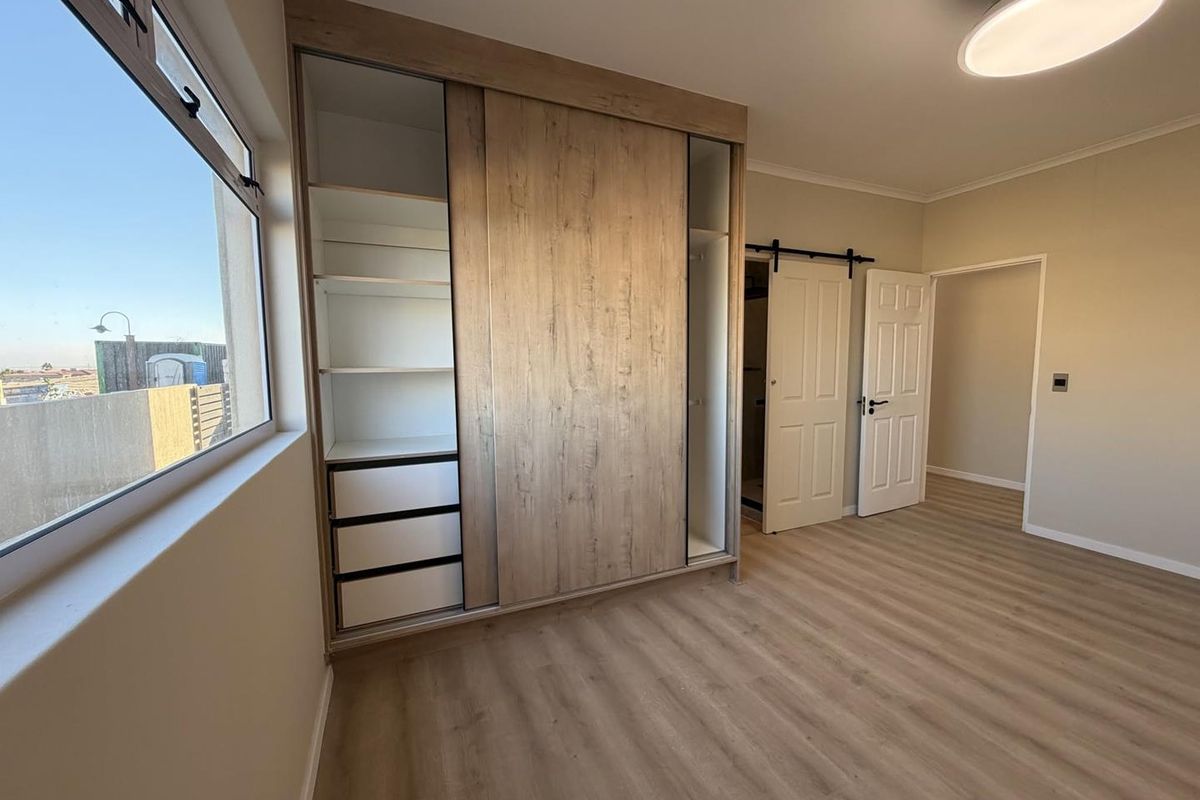 A bright, modern bedroom featuring light wood-look laminate flooring, a large built-in sliding wardrobe, and a stylish barn door leading to an en-suite.