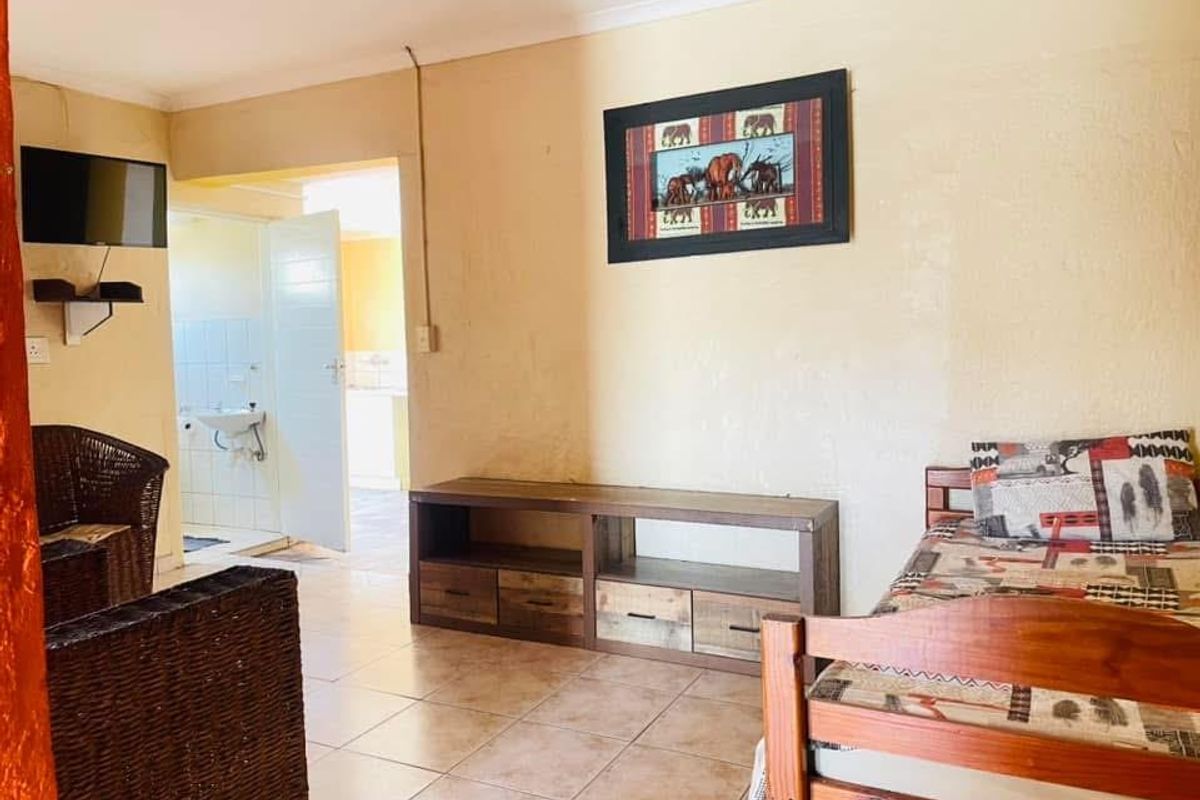 A living area featuring tiled flooring and neutral walls, with an adjacent view into a functional kitchen space.