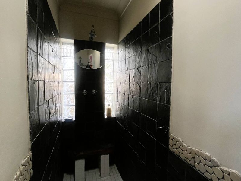 A compact shower enclosure featuring dark slate wall tiles, a pebble mosaic border, and a glass block window providing natural light.