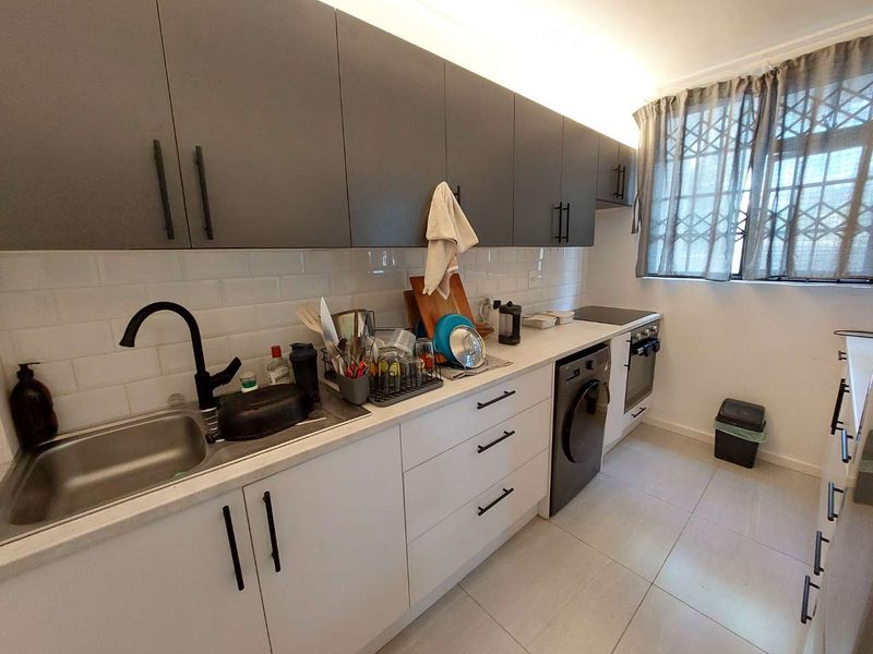 Modern kitchen featuring two-tone cabinetry, subway tile backsplash, integrated appliances, and tiled flooring with a window security gate.