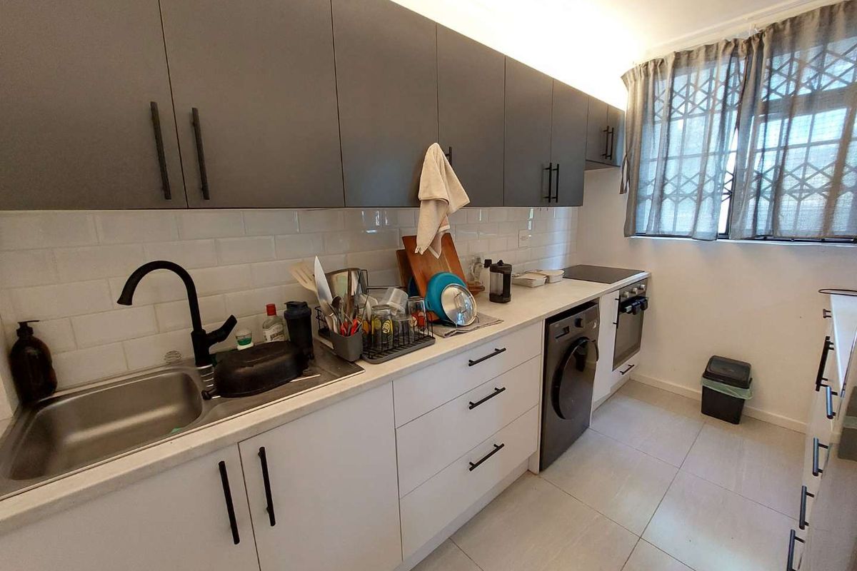Modern kitchen featuring two-tone cabinetry, subway tile backsplash, integrated appliances, and tiled flooring with a window security gate.