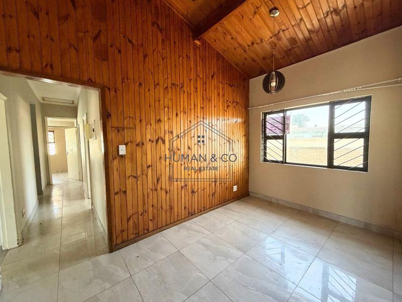 Spacious living area featuring a vaulted timber ceiling, wood-paneled feature wall, and neutral tiled flooring with large windows for natural light.