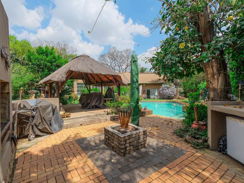Outdoor entertainment area featuring a swimming pool, thatched lapa, built-in braai, and brick-paved patio space.