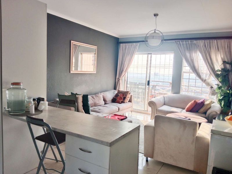 Open-plan living area featuring a breakfast bar, tiled flooring, and sliding glass doors leading to a balcony with city views.