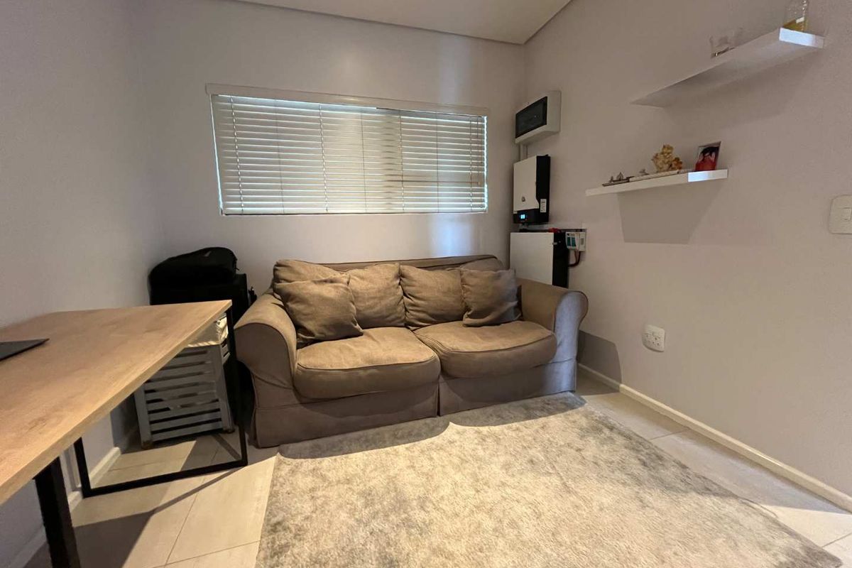 A functional living room featuring a window with blinds, wall-mounted shelving, and integrated electrical infrastructure including an inverter system.