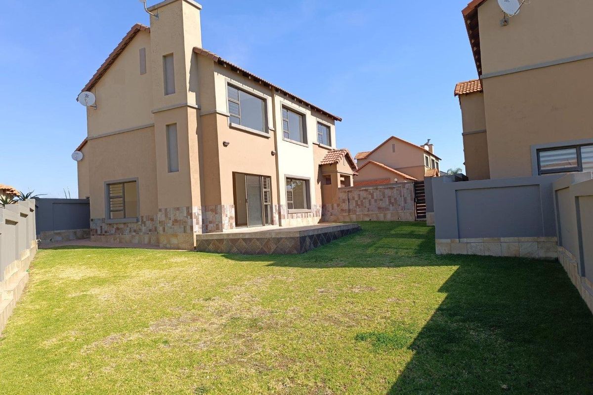 Rear view of the house featuring a private garden, a paved patio area, and stone-clad exterior detailing.