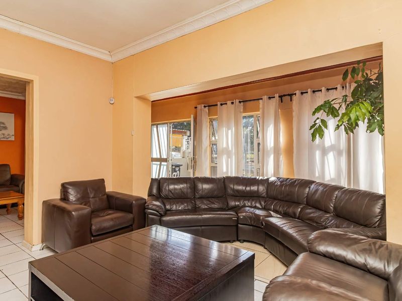 A spacious living room featuring tiled flooring, decorative cornicing, and large windows that allow for ample natural light.