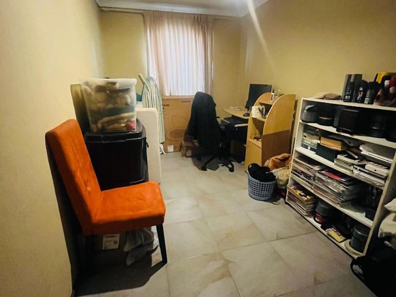 A compact bedroom featuring tiled flooring and neutral wall finishes, currently utilized as a multi-purpose storage and workspace area.