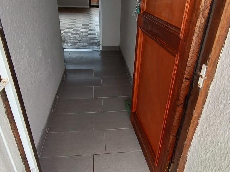 An entry hallway featuring tiled flooring, a timber door, and a security gate, leading into the main living area of the apartment.