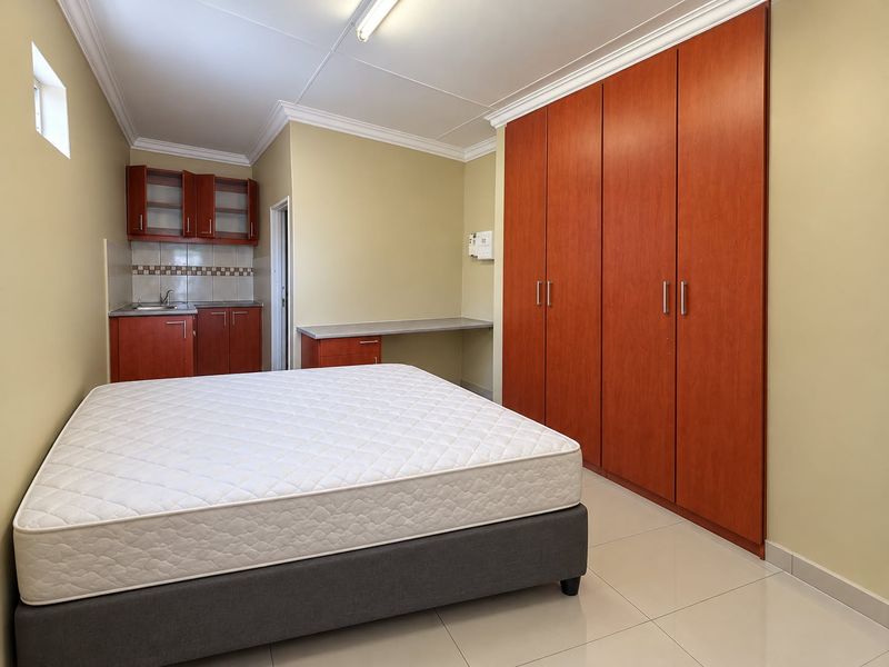 A bedroom featuring built-in cupboards, a compact kitchenette with sink, and a built-in desk area, finished with tiled flooring and crown molding.