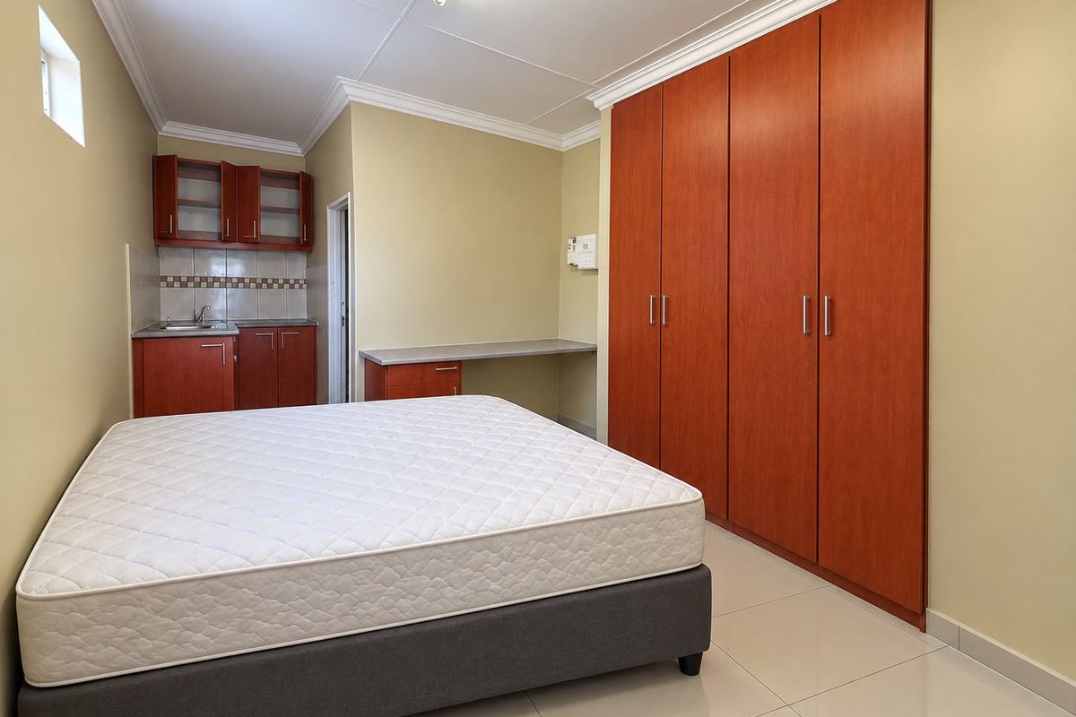 A bedroom featuring built-in cupboards, a compact kitchenette with sink, and a built-in desk area, finished with tiled flooring and crown molding.