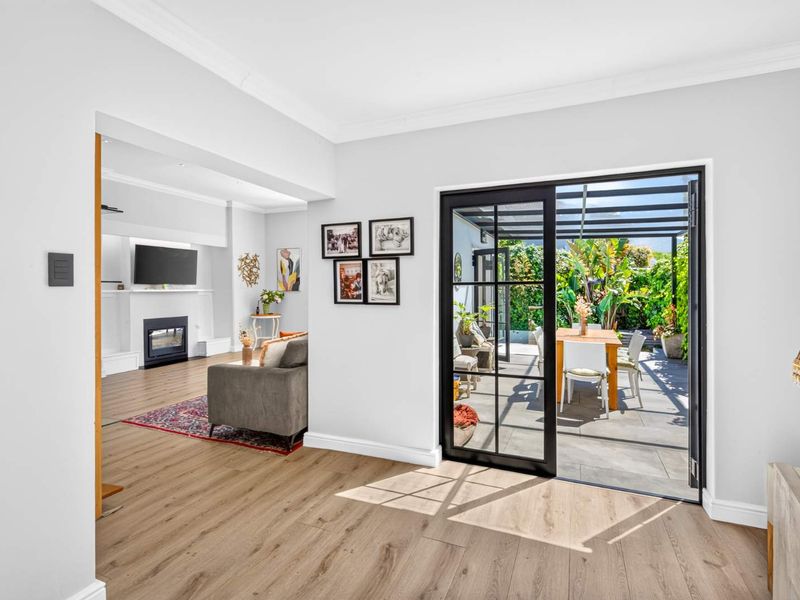 Bright living area featuring modern laminate flooring, crown molding, and seamless access to a covered outdoor patio through black-framed glass doors.