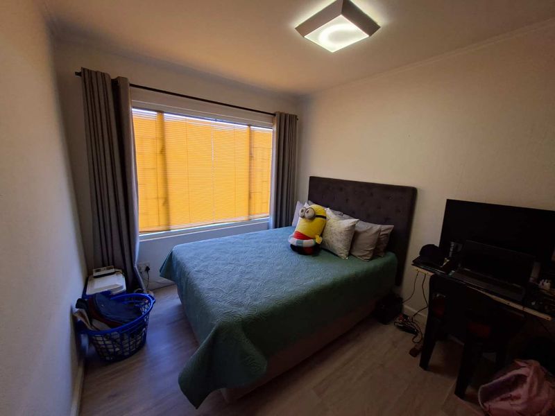 A functional bedroom featuring laminate flooring, a central ceiling light, and a window fitted with blinds.