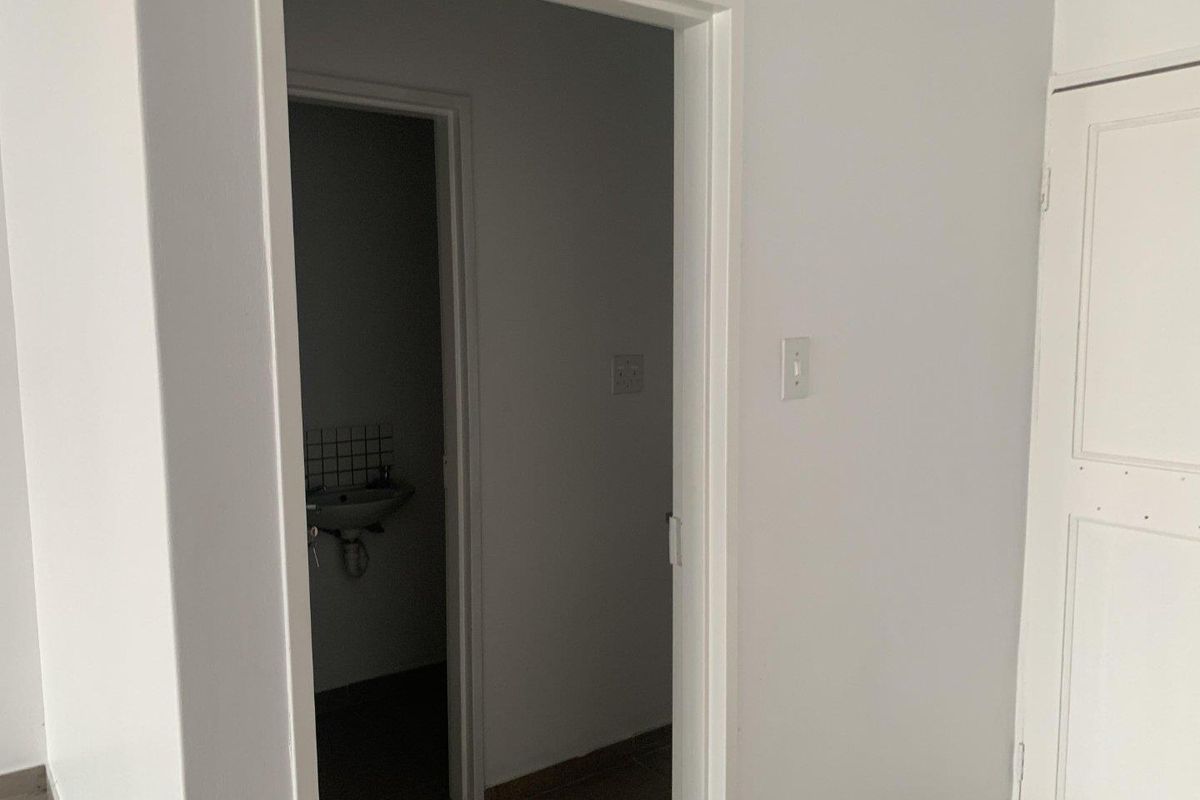 A view through a doorway into a small, empty bathroom featuring a wall-mounted basin with a tiled splashback.
