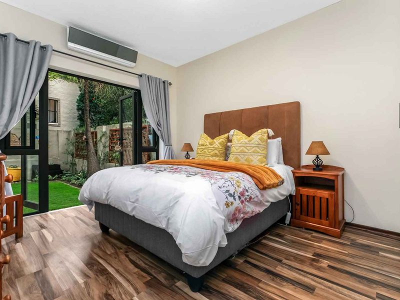 A well-lit bedroom featuring laminate flooring, a built-in wardrobe, and a sliding glass door providing direct access to a private garden area.