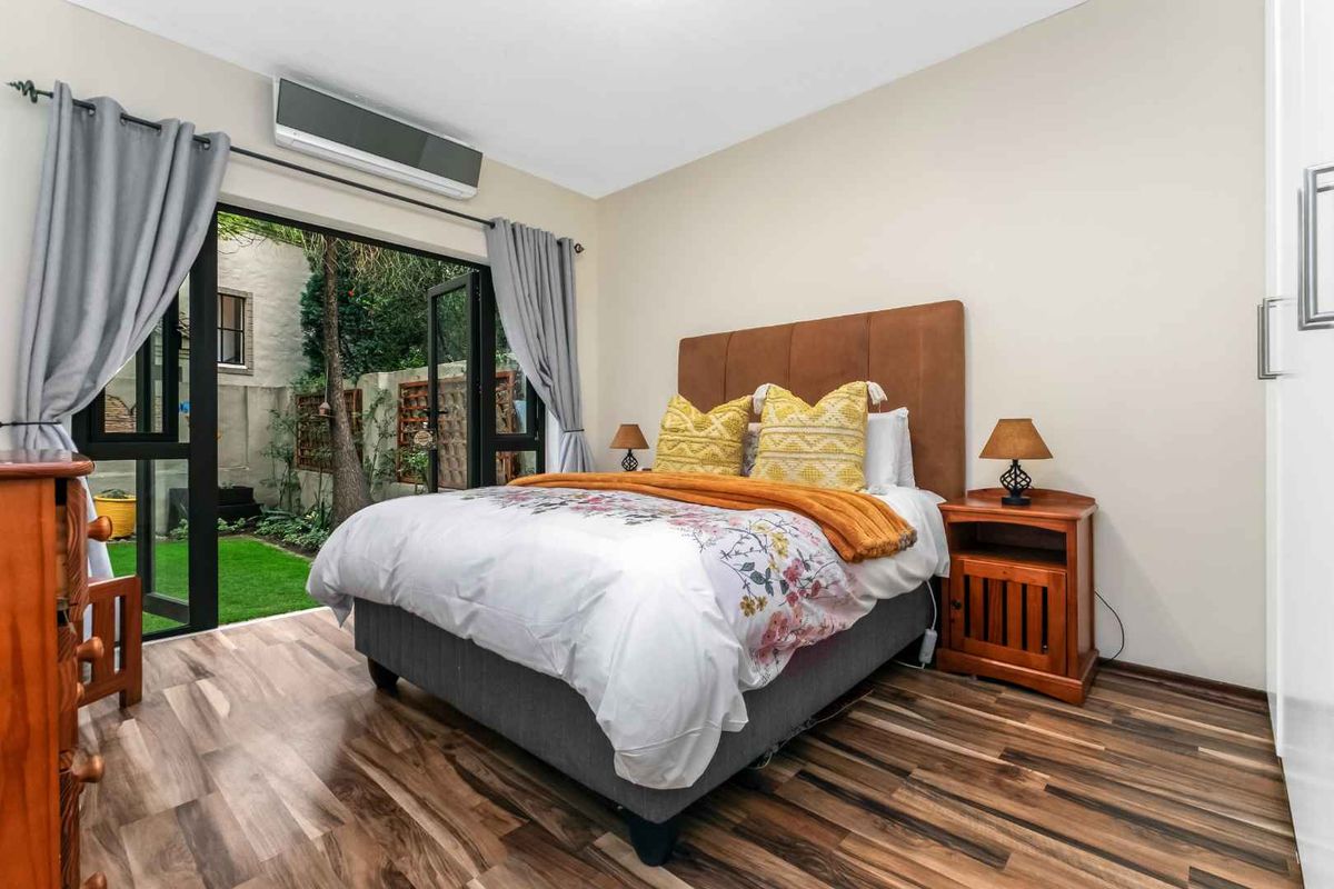 A well-lit bedroom featuring laminate flooring, a built-in wardrobe, and a sliding glass door providing direct access to a private garden area.